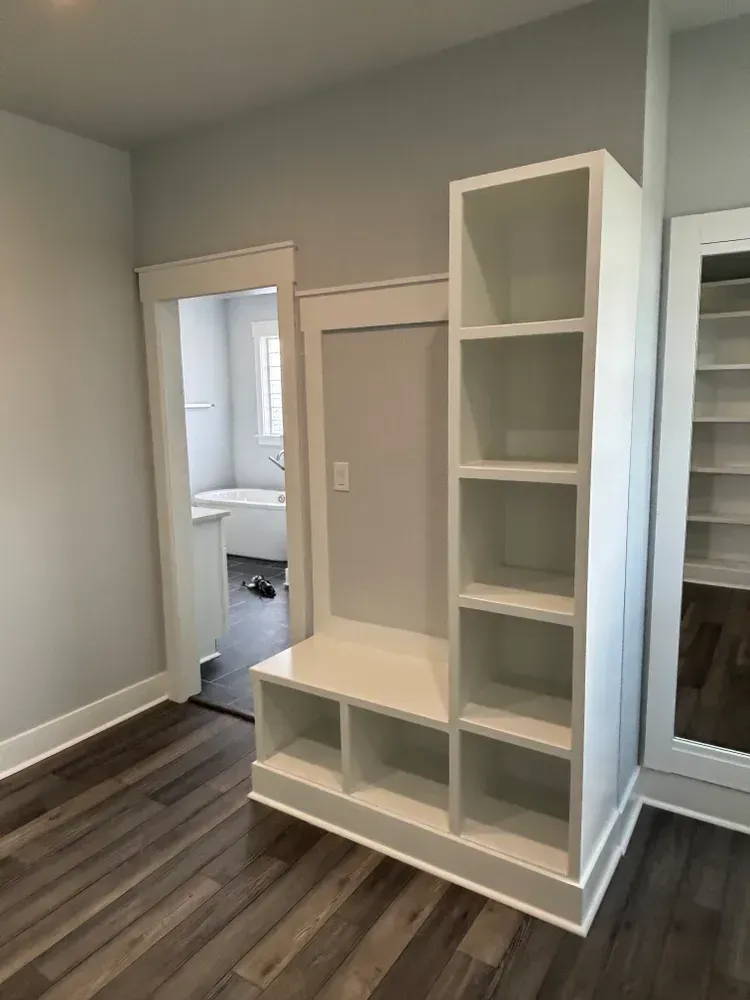 Modern bedroom nook with white shelving and built-in storage against gray walls and dark wood flooring