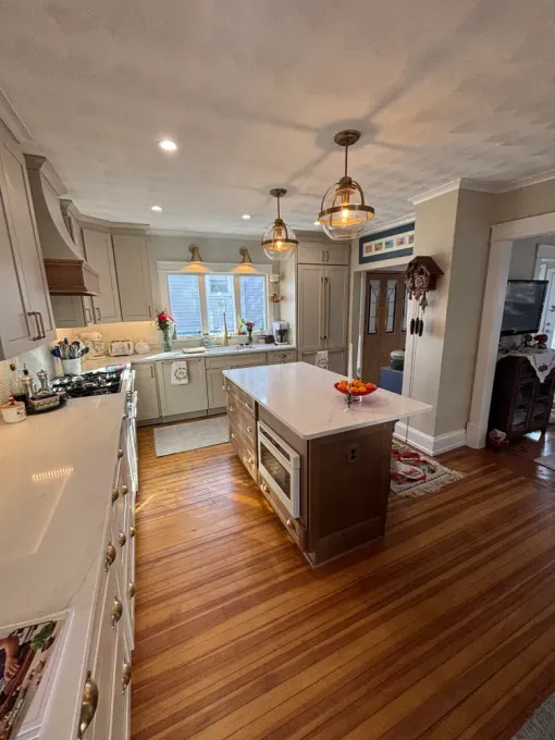 Bright kitchen with white cabinets, a central island, wood floors, and pendant lights near a window.