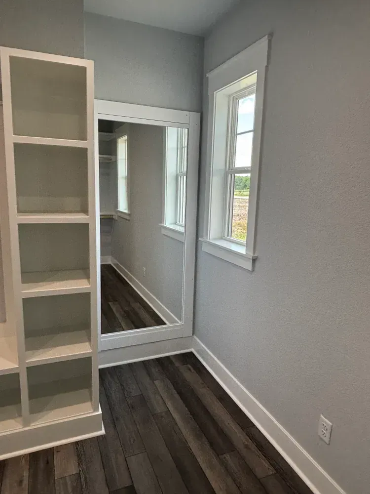 Empty gray room with dark wood floors, a window, and a mirrored closet door.