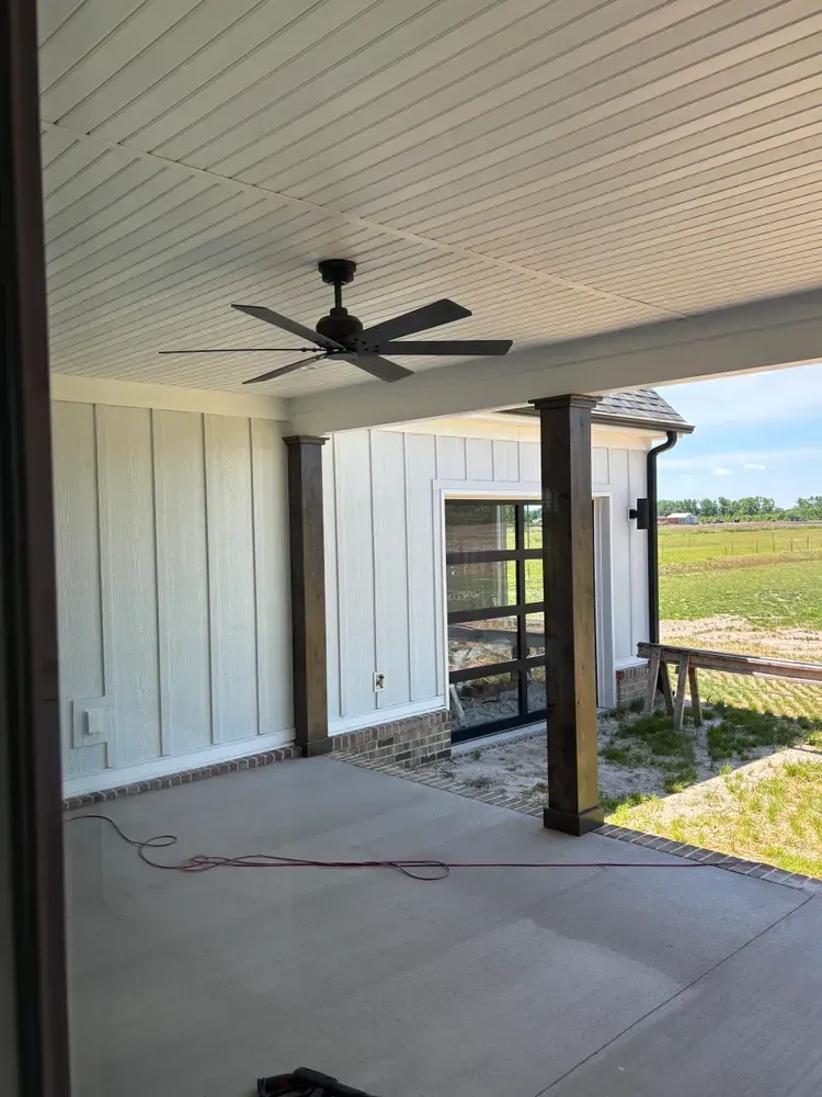 Covered patio with ceiling fan, concrete floor, and open view of a yard and fields