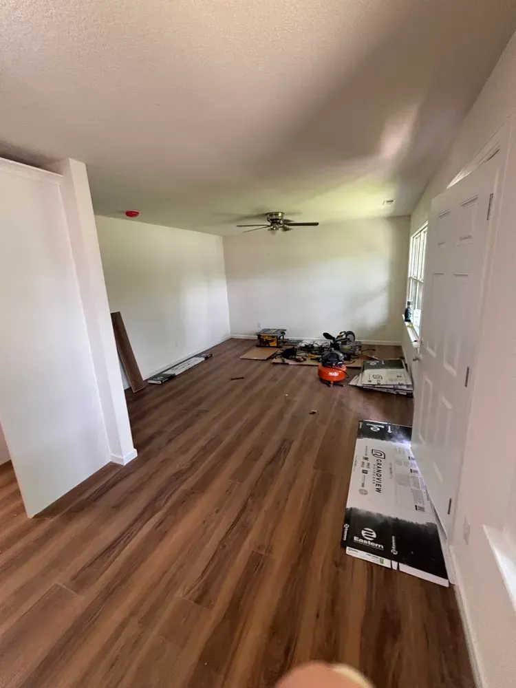Empty bedroom with wood floors, white walls, ceiling fan, and scattered renovation materials.