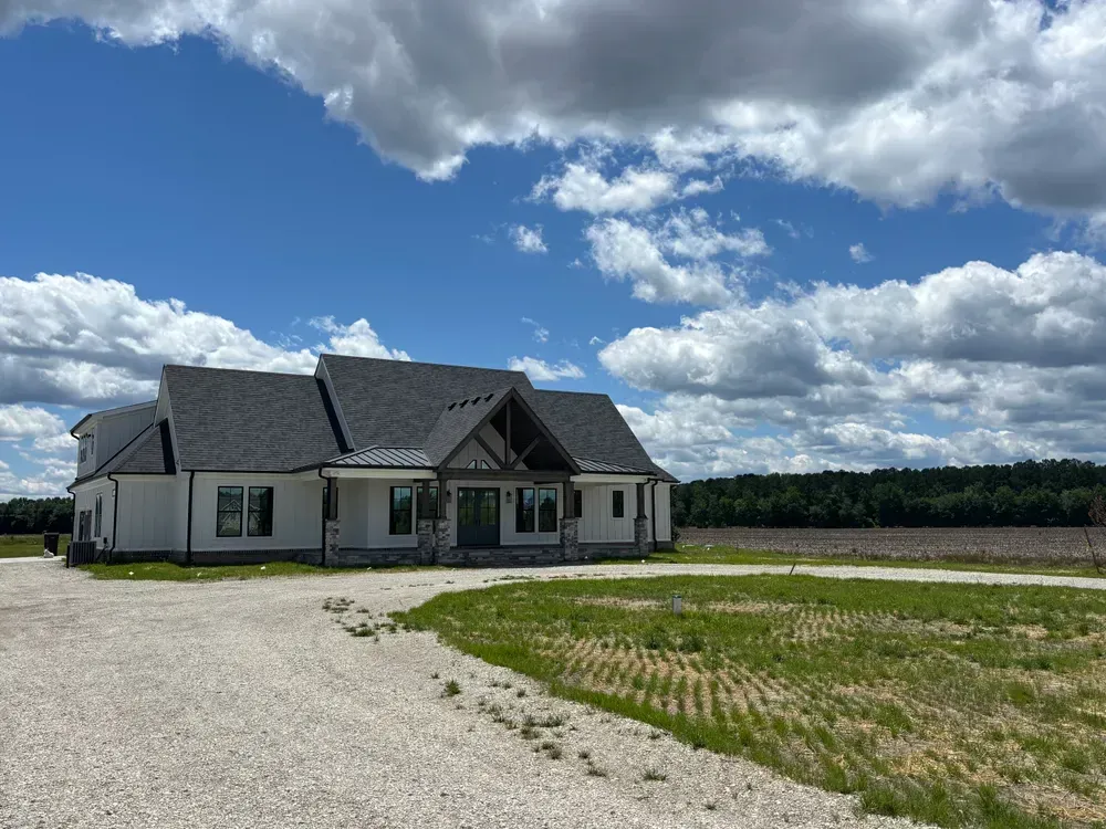 White house with a gray roof on a gravel lot under a bright blue sky with clouds