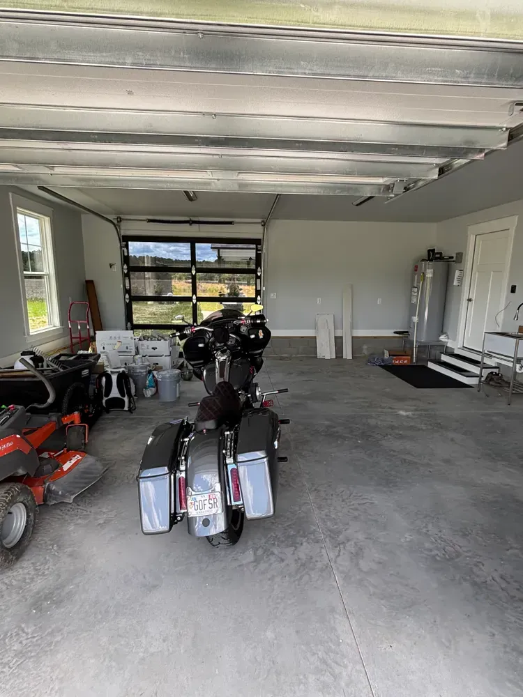 Garage interior with several motorcycles and ATVs parked on a concrete floor, open garage door at the back.