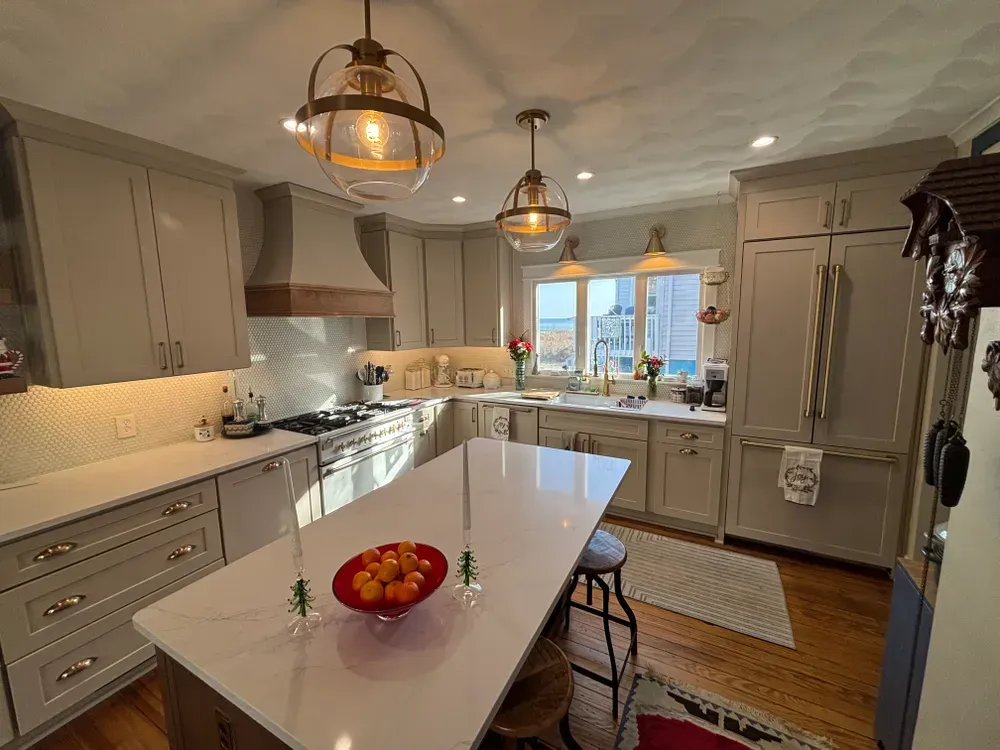 Bright modern kitchen with gray cabinets, white island, pendant lights, and fruit bowl on the counter