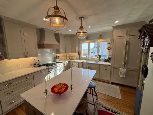 Bright modern kitchen with gray cabinets, white island, pendant lights, and fruit bowl on the counter