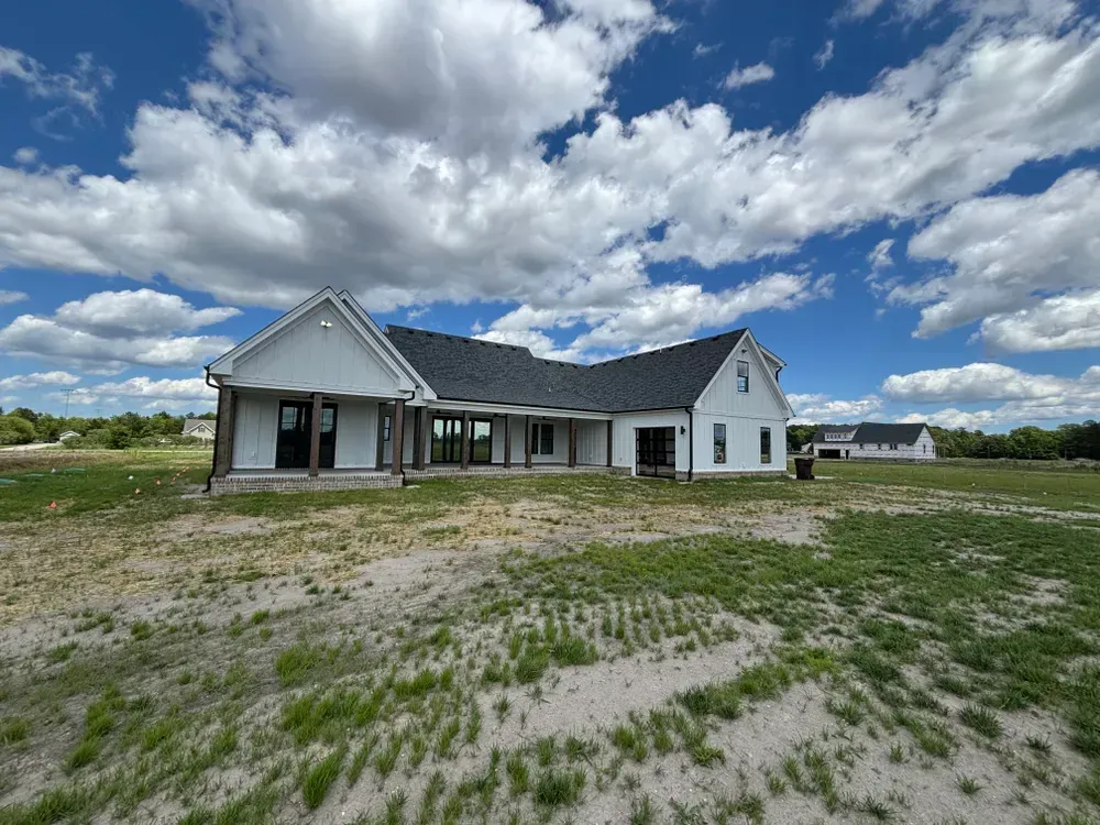 New white house with dark roof on a sandy lot under a cloudy blue sky