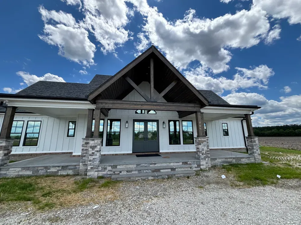 Modern single-story house with stone accents, front porch, and gravel driveway under a cloudy sky