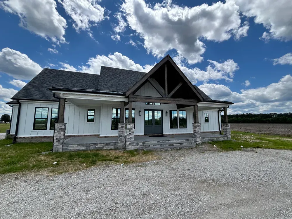 Modern farmhouse-style building with gray roof and stone accents under a cloudy blue sky
