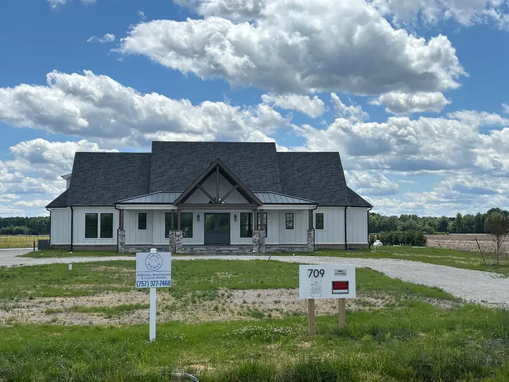 White house with dark roof on a grassy lot under a cloudy sky, with real estate signs in front