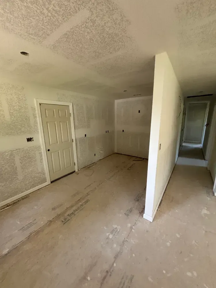 Empty unfinished room with beige walls, white doors, and bare subfloor, viewed from a hallway.