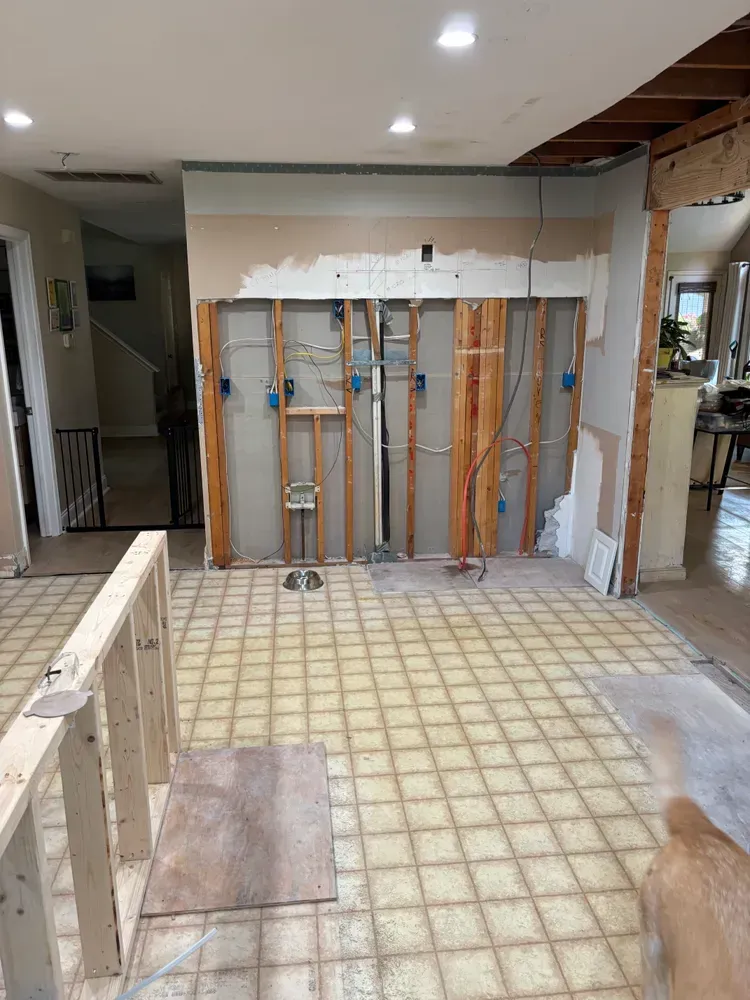 Kitchen under renovation with exposed wall framing, open plumbing, and a tiled floor.