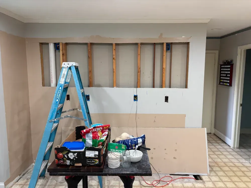 Partially renovated room with ladder, exposed wall studs, and construction materials on the floor