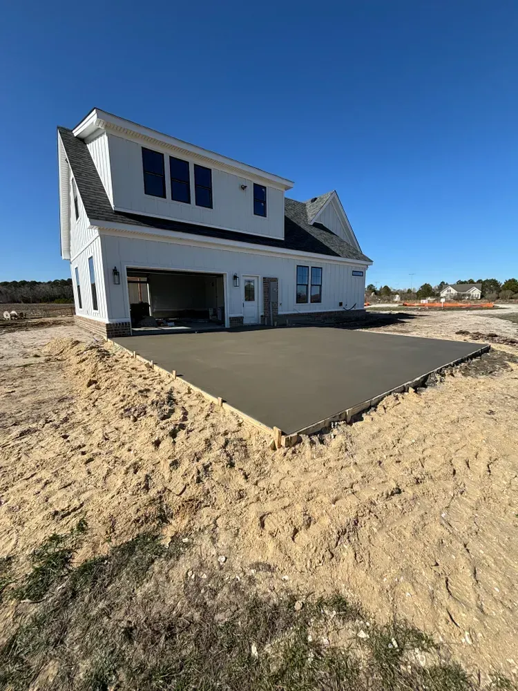 Newly built white two-story house with a large concrete driveway under a clear blue sky