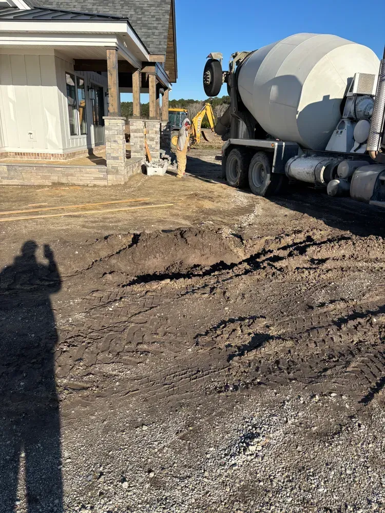 Construction site with cement mixer truck beside a house and a large dirt excavation in the foreground