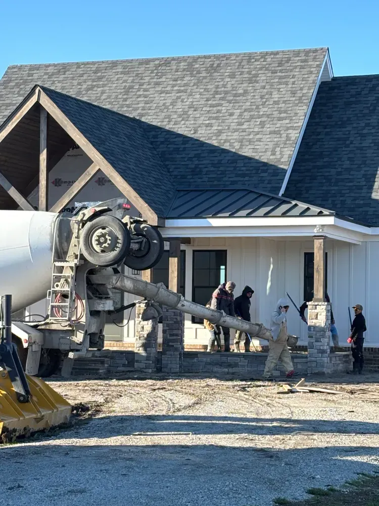 Construction workers pouring concrete beside a house under construction, with a cement mixer in the foreground