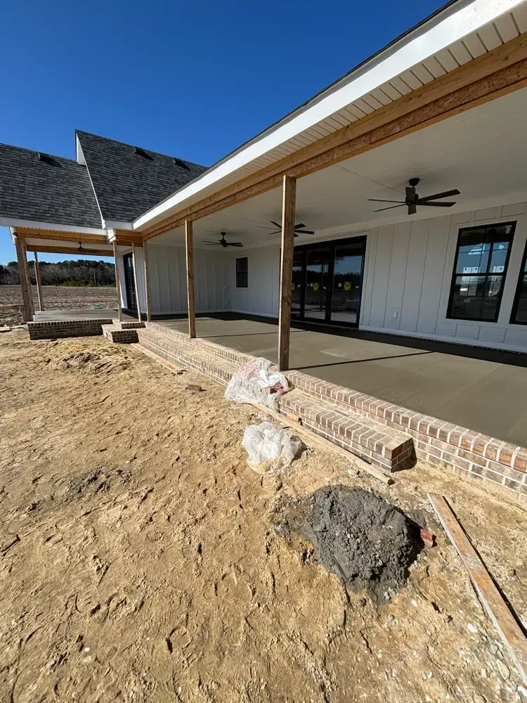 Newly built house with covered porch and rough dirt yard under a clear blue sky