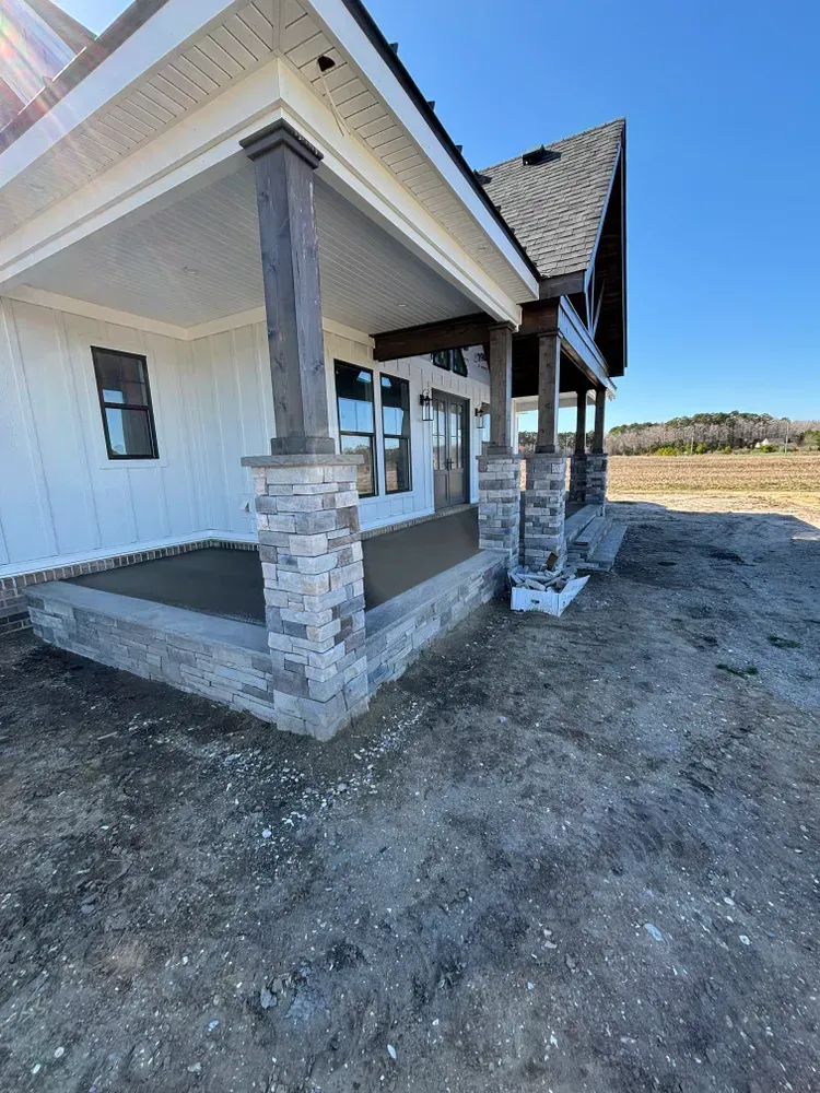 New house porch with stone columns and white siding under construction in a dirt lot
