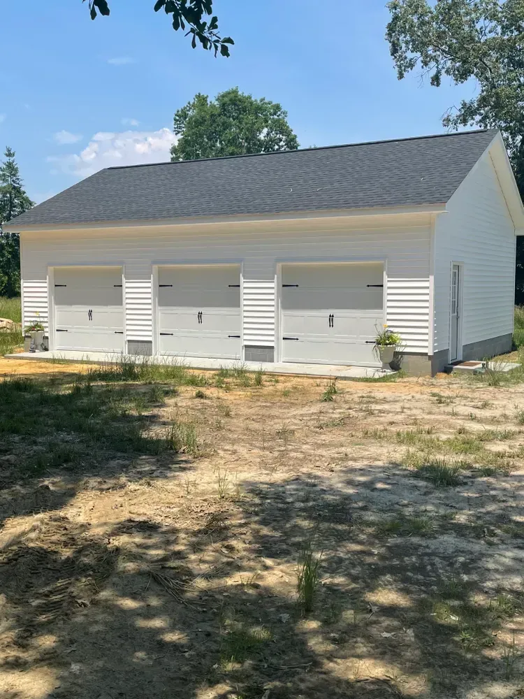 Three-bay white garage with gray roof and closed doors in a sunny yard.