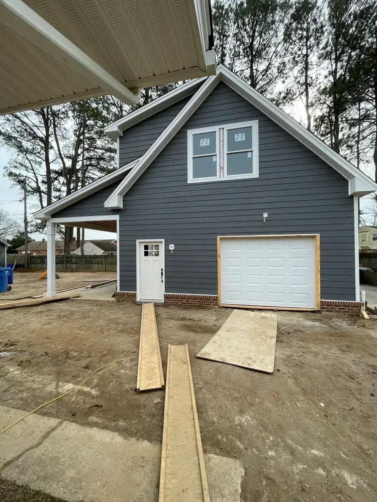 Gray house with garage and double windows, viewed from a dirt driveway under construction