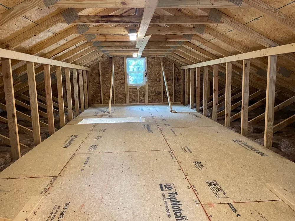 Orange construction lift beside a gray house with new gable framing under the roof.