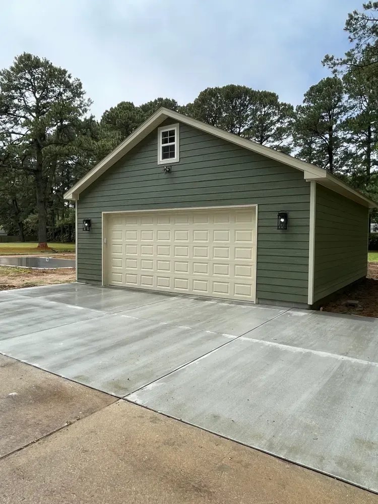 Green garage with beige door and concrete driveway in a wooded area
