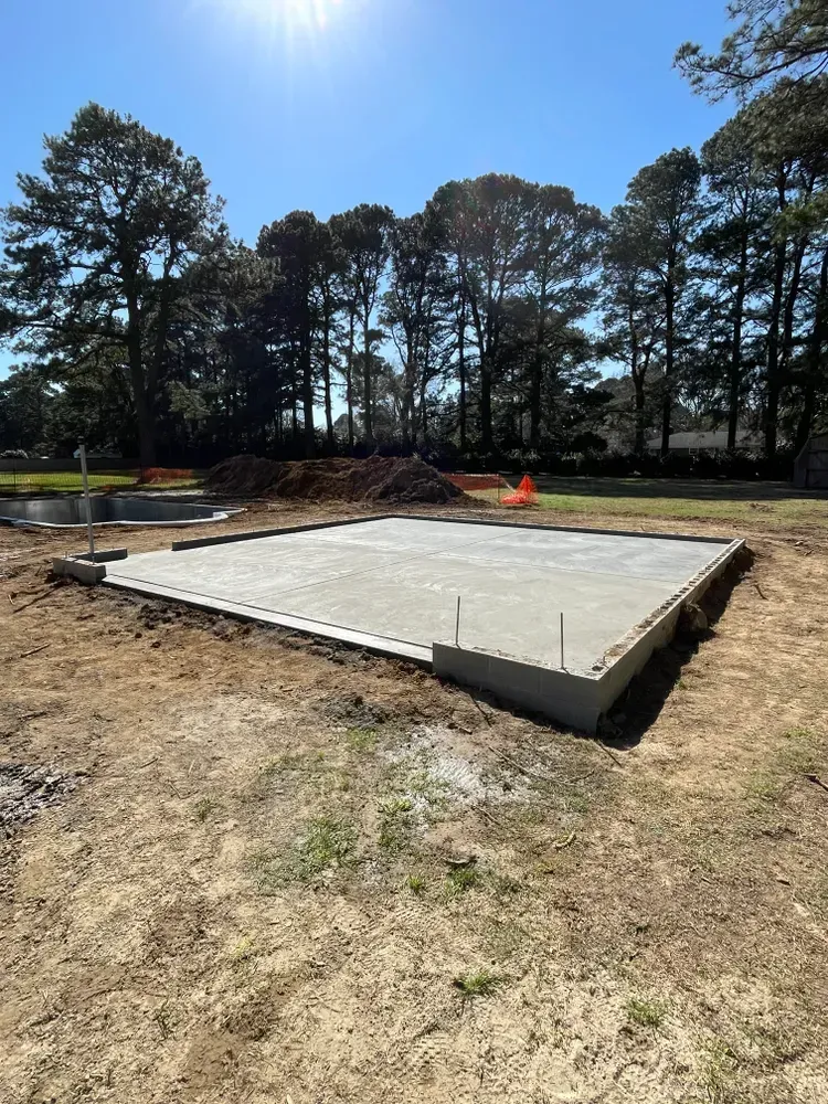 Fresh concrete slab foundation at a construction site with trees and bright sun in the background