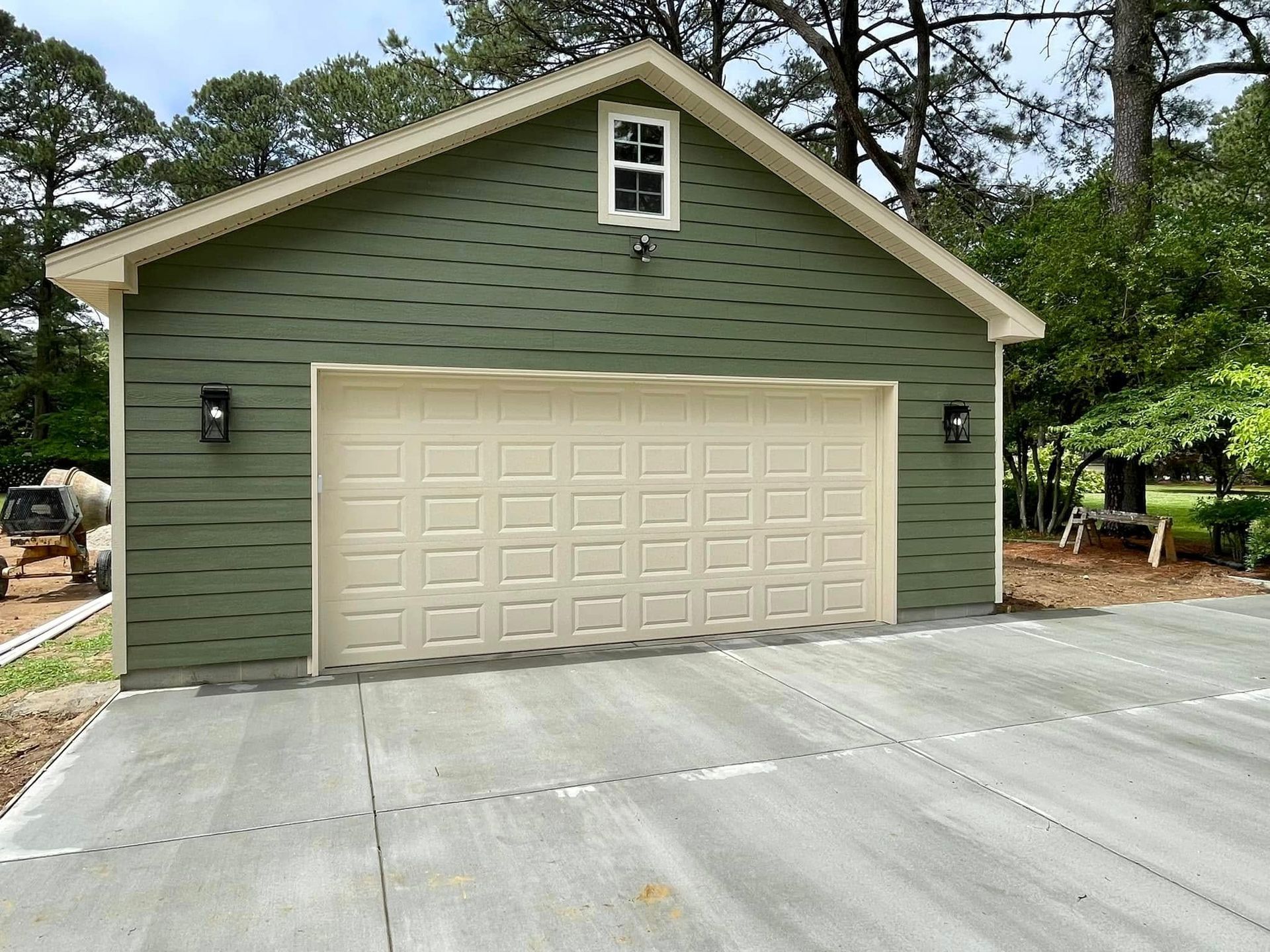 Green garage with beige double doors and a concrete driveway.