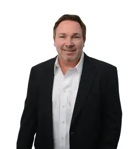 A man in a suit and white shirt is standing in front of a white background.