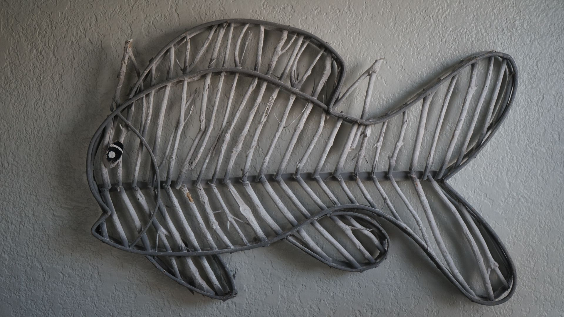 A fish made of wire is hanging on a wall.