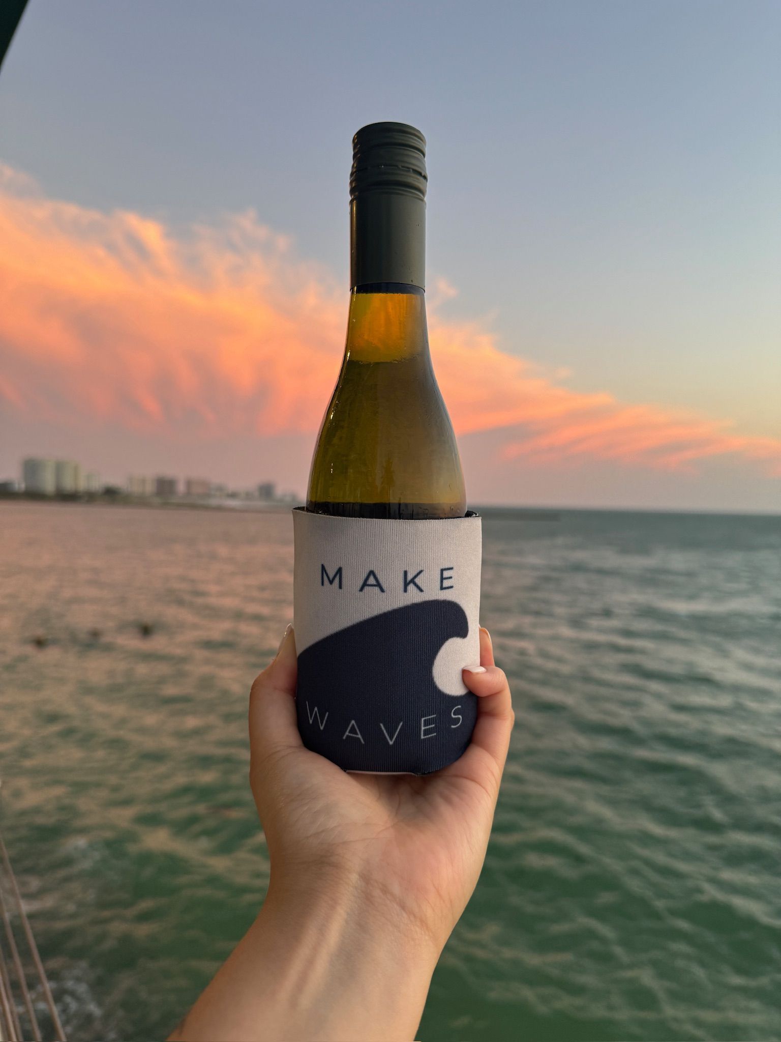 A person is holding a bottle of wine in front of the ocean.