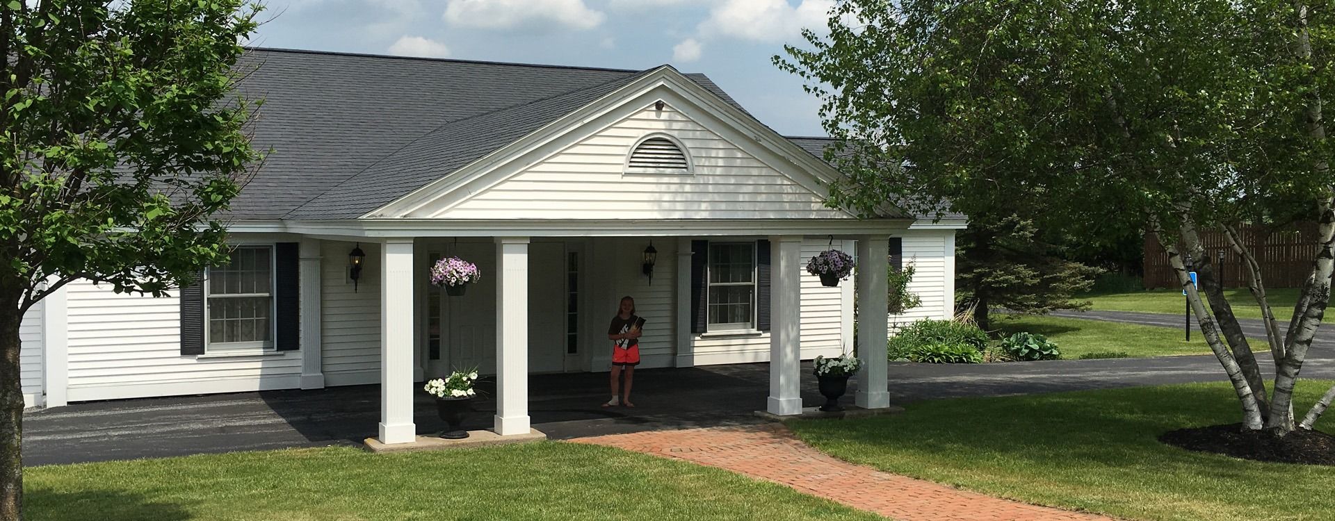 A white house with a covered porch; a person stands in front.