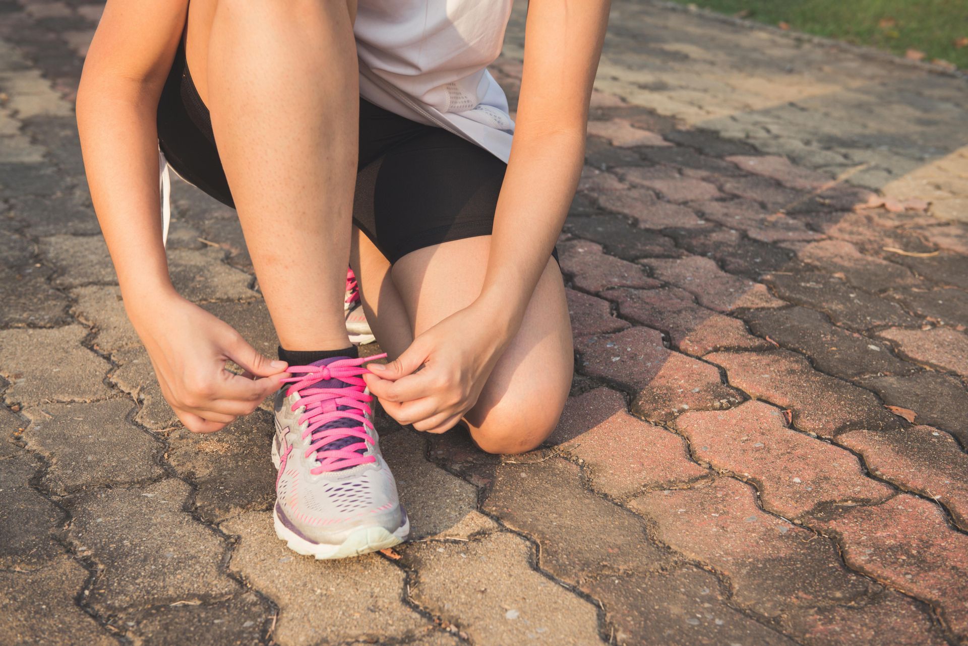 A woman is tying her shoes on a brick sidewalk.
