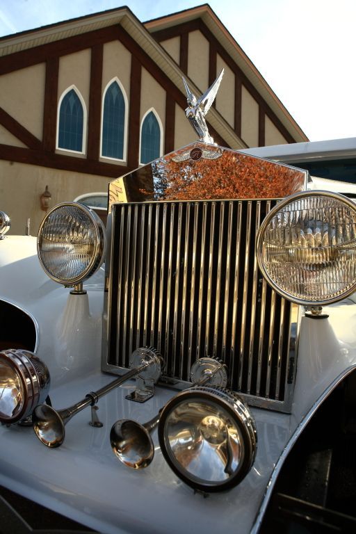 A white rolls royce is parked in front of a building