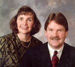 A man and a woman are posing for a picture together . the man is wearing a suit and tie.