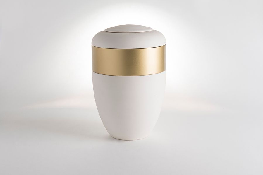 A white vase with a gold stripe on the side is sitting on a white surface.