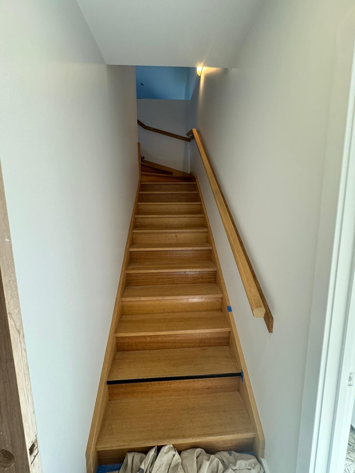 Wooden staircase with handrails ascending between white walls, leading to a blue ceiling — Andrew Harper Painting & Decorating in Albury, NSW