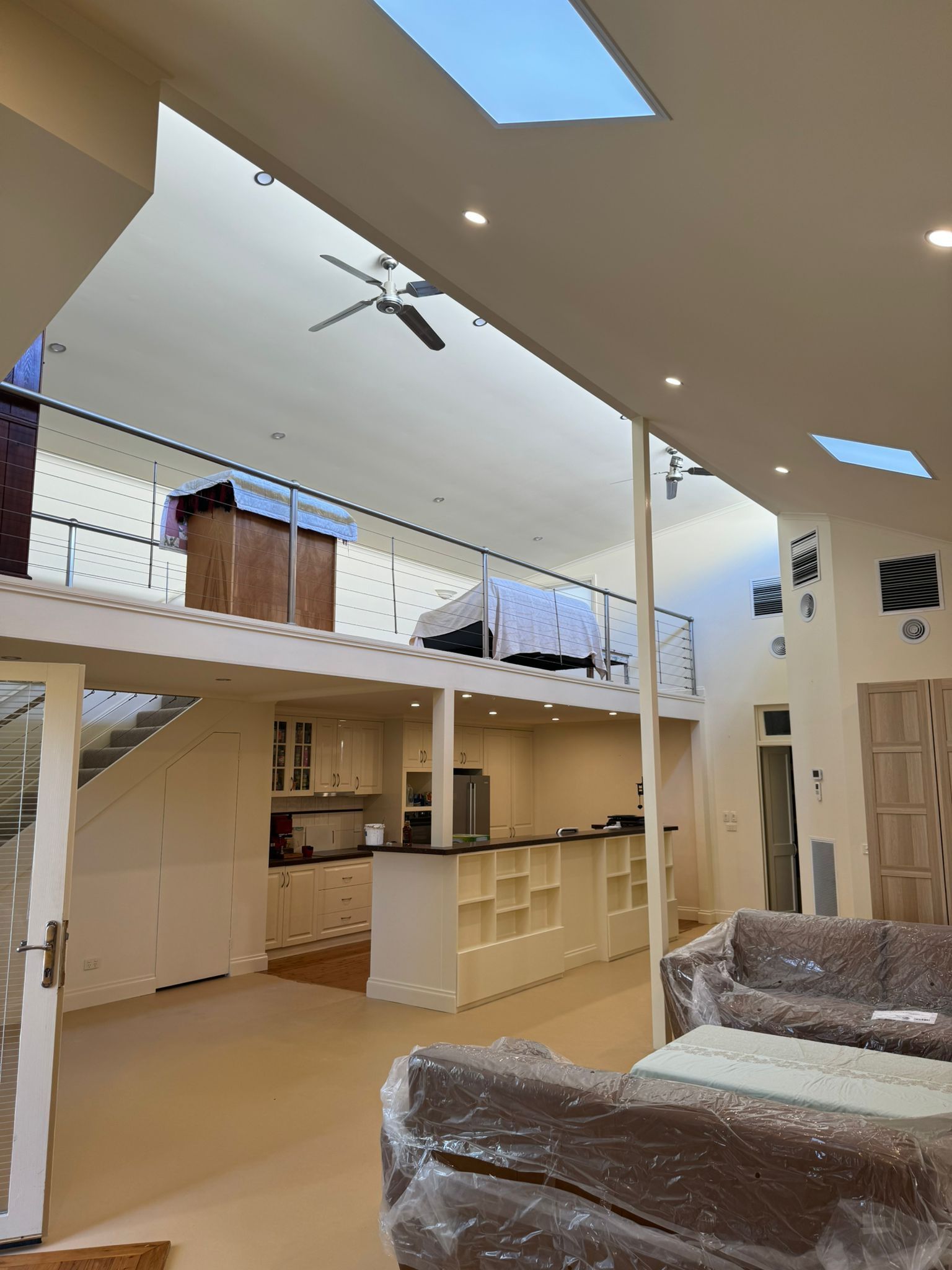 Interior of a modern home with a mezzanine. White walls, skylights, kitchen island, sofa covered in plastic — Andrew Harper Painting & Decorating in Albury, NSW