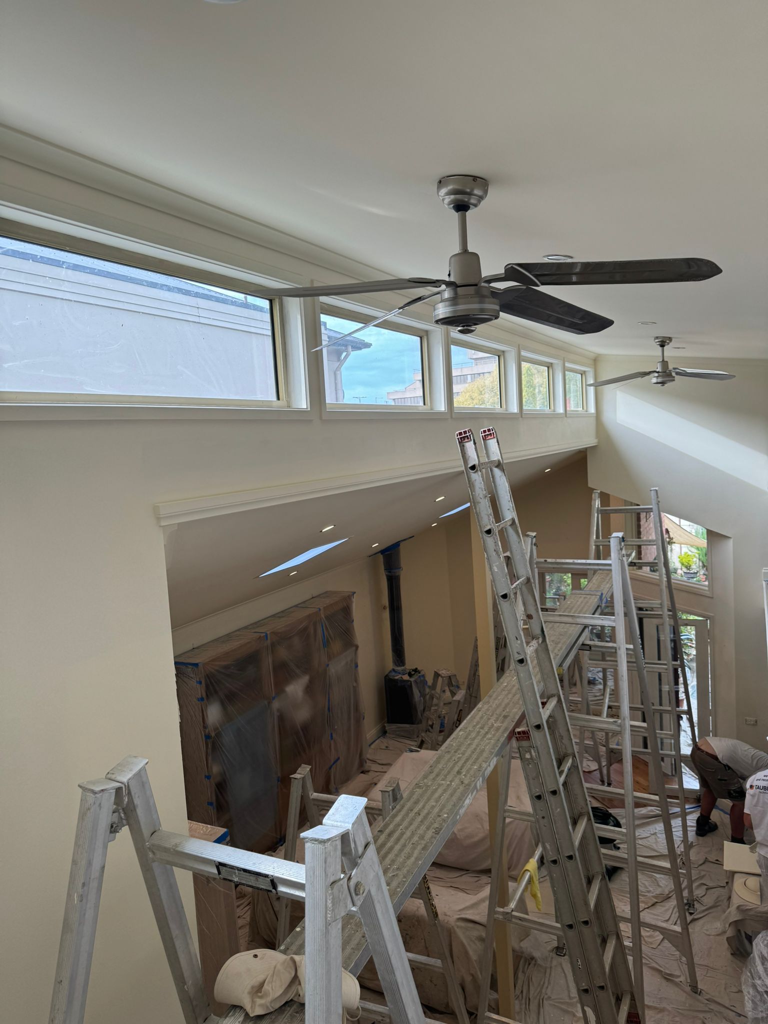 Interior with high ceiling, windows, ceiling fans, and ladders, suggesting renovation in progress — Andrew Harper Painting & Decorating in Albury, NSW