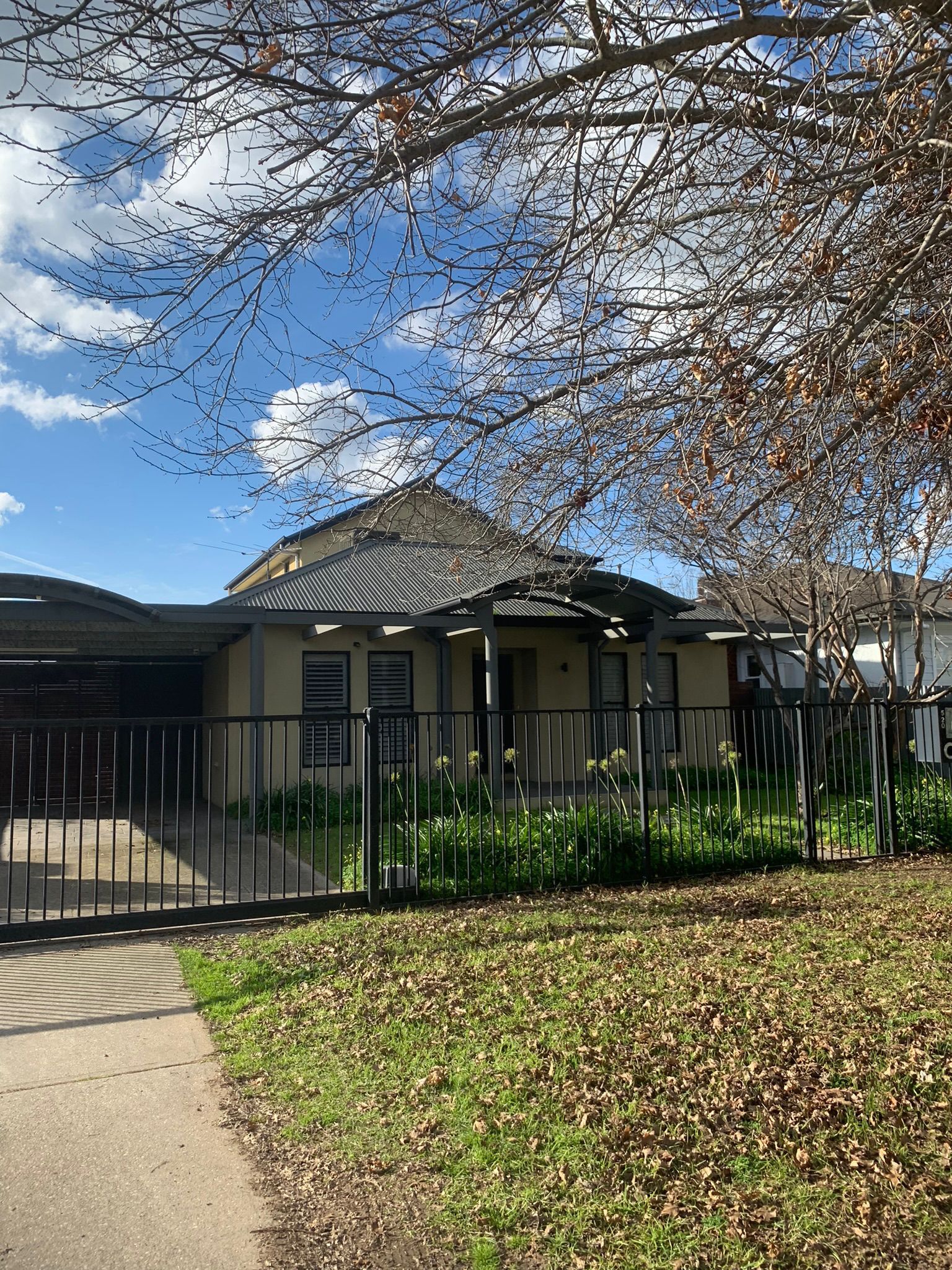 Yellow house with black fence and carport, surrounded by a lawn and trees under a blue sky — Andrew Harper Painting & Decorating in Albury, NSW