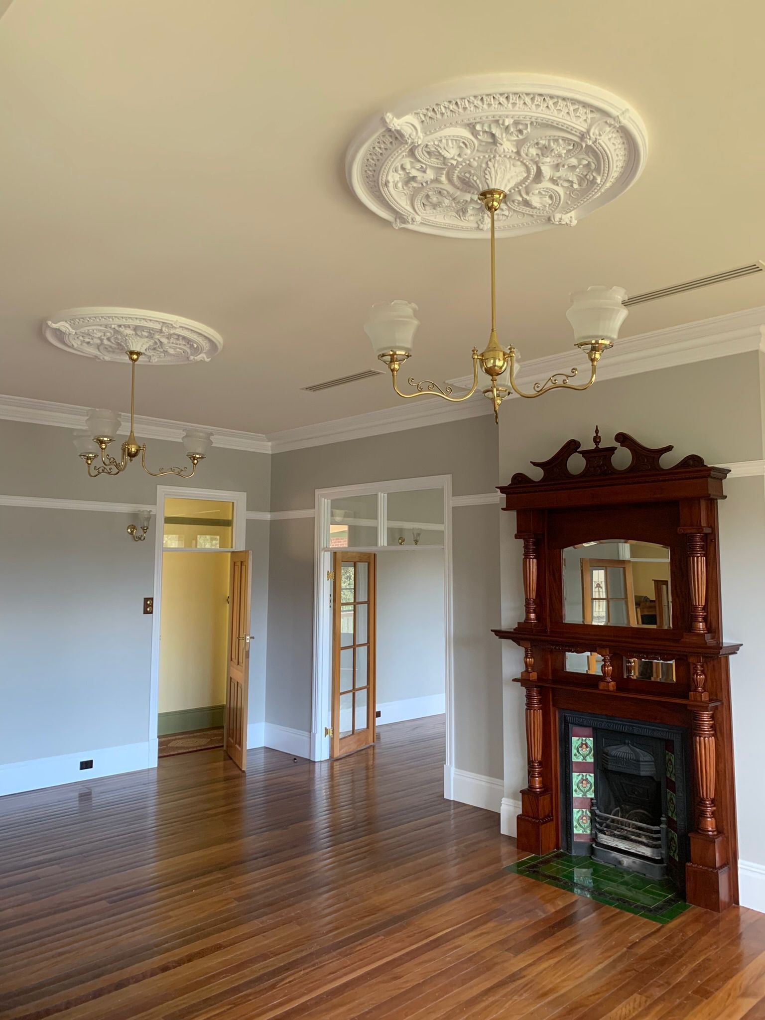 Empty room with a fireplace, ornate ceiling medallions, chandeliers, and hardwood floors — Andrew Harper Painting & Decorating in Albury, NSW