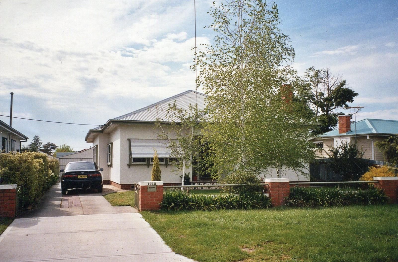 A white bungalow with a driveway and car, set behind a brick and wrought iron fence, on a green lawn — Andrew Harper Painting & Decorating in Albury, NSW