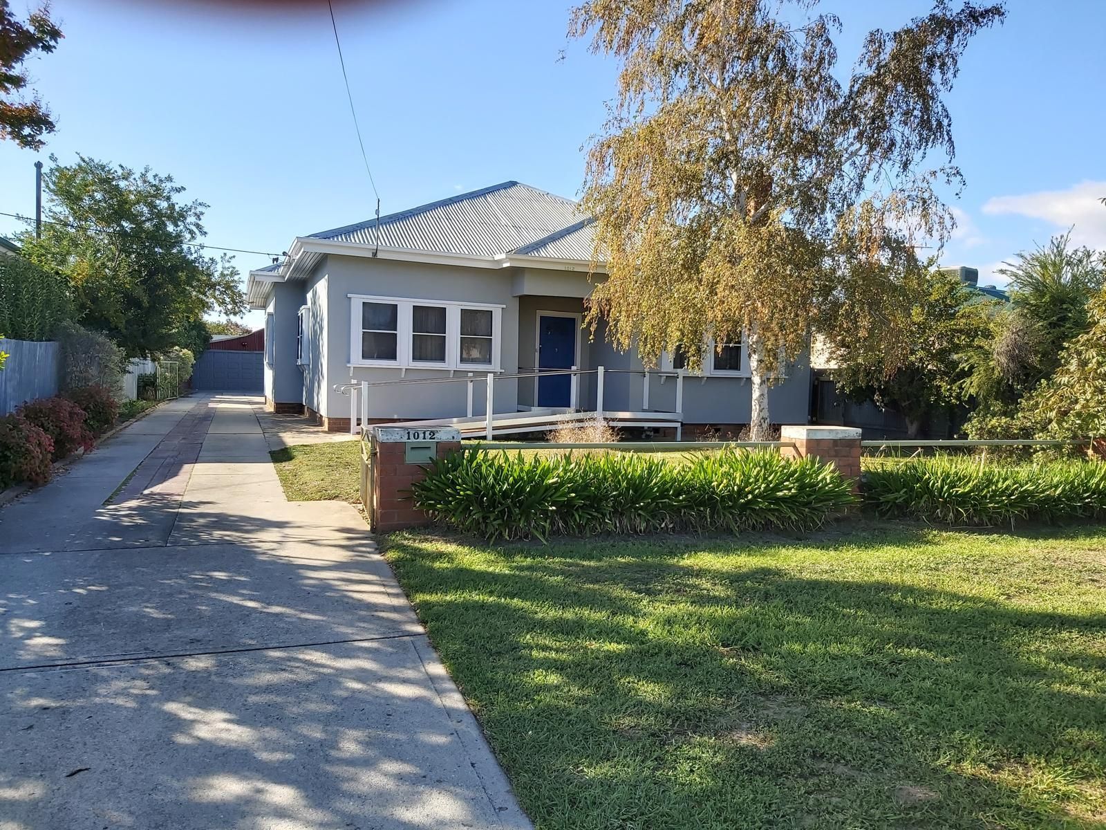 Grey house with blue door and a driveway. Sunny day with trees and lawn — Andrew Harper Painting & Decorating in Albury, NSW