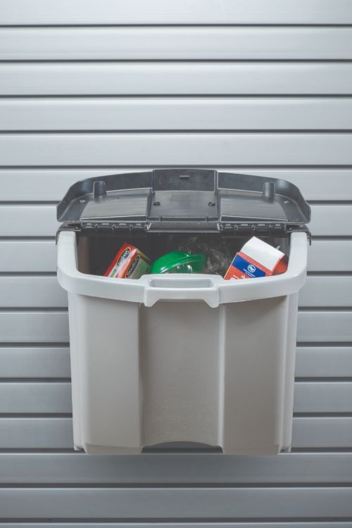 A white bin filled with groceries is hanging on a wall.