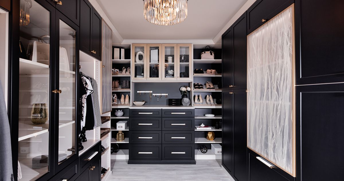 A walk in closet with black cabinets , drawers , shelves and a chandelier.