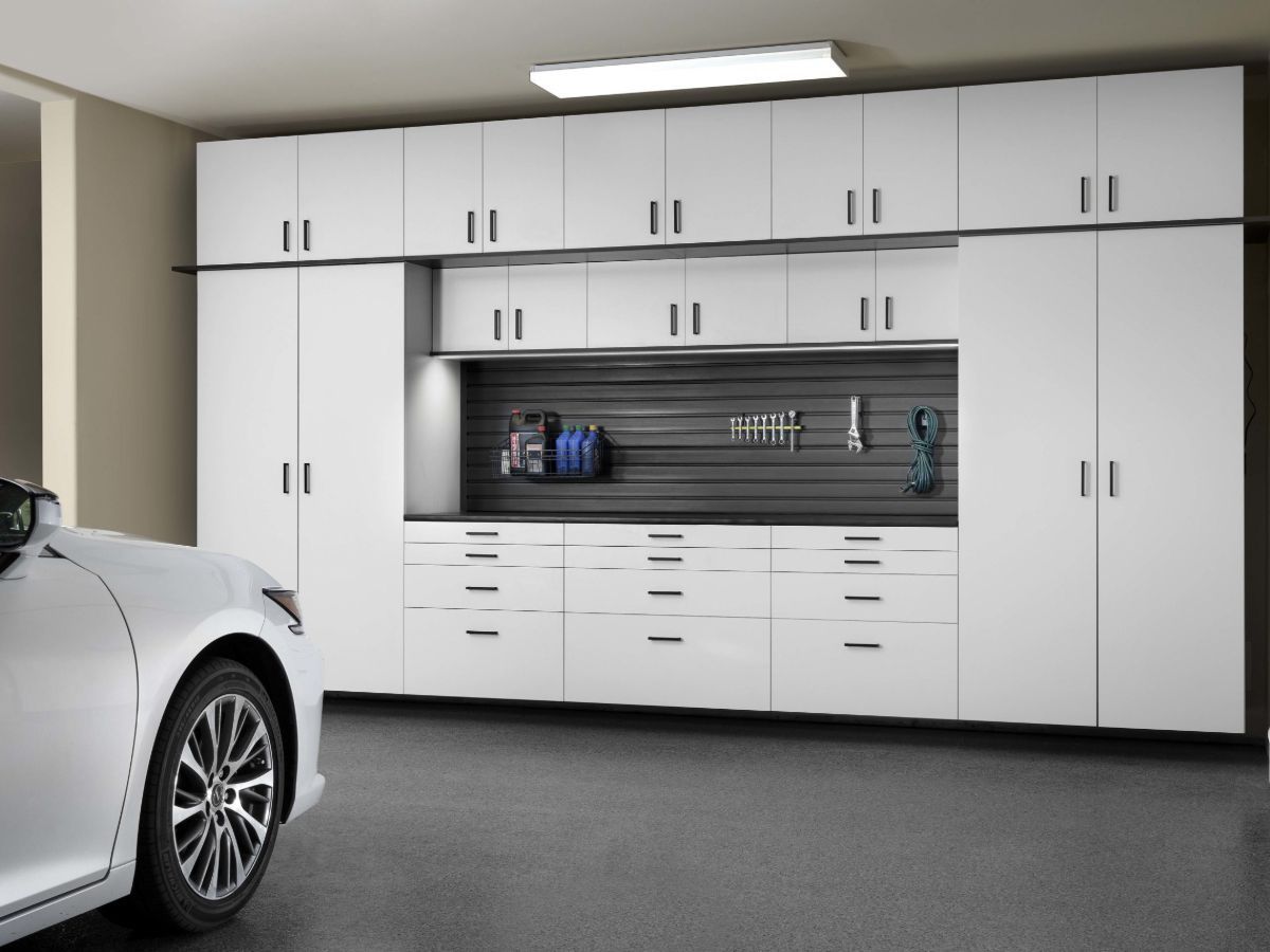 A white car is parked in a garage with white cabinets