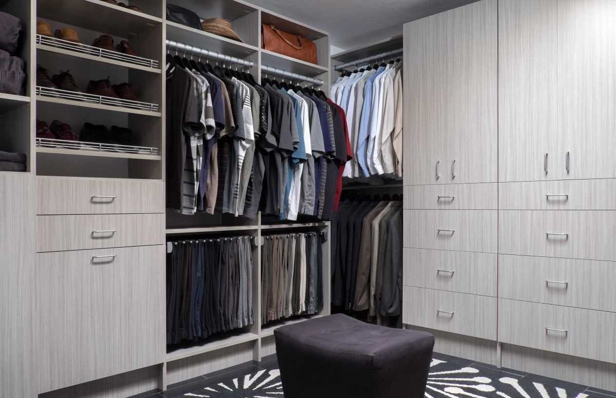 A walk in closet filled with lots of clothes and a black ottoman.