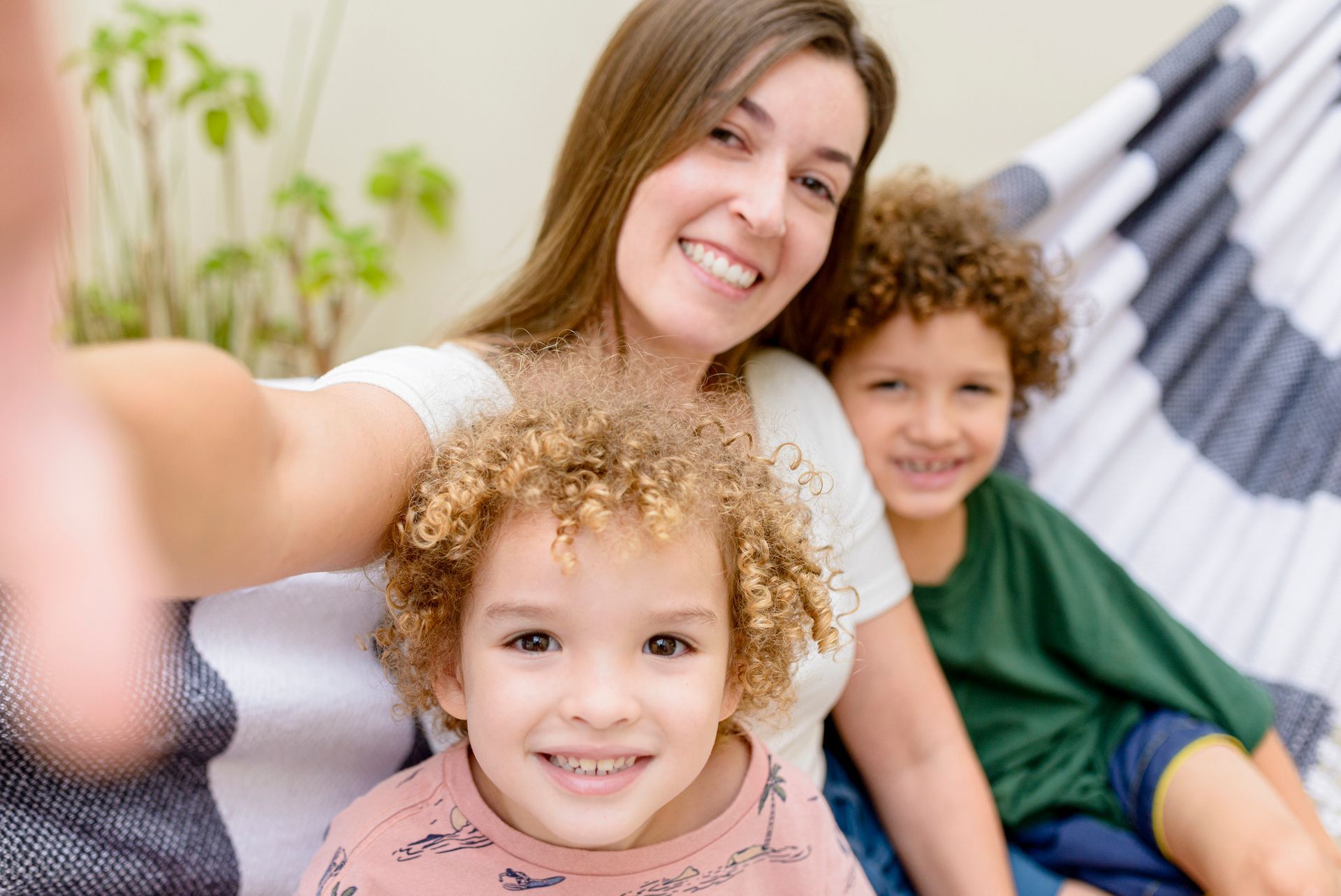 A woman is taking a selfie with two children in a hammock.