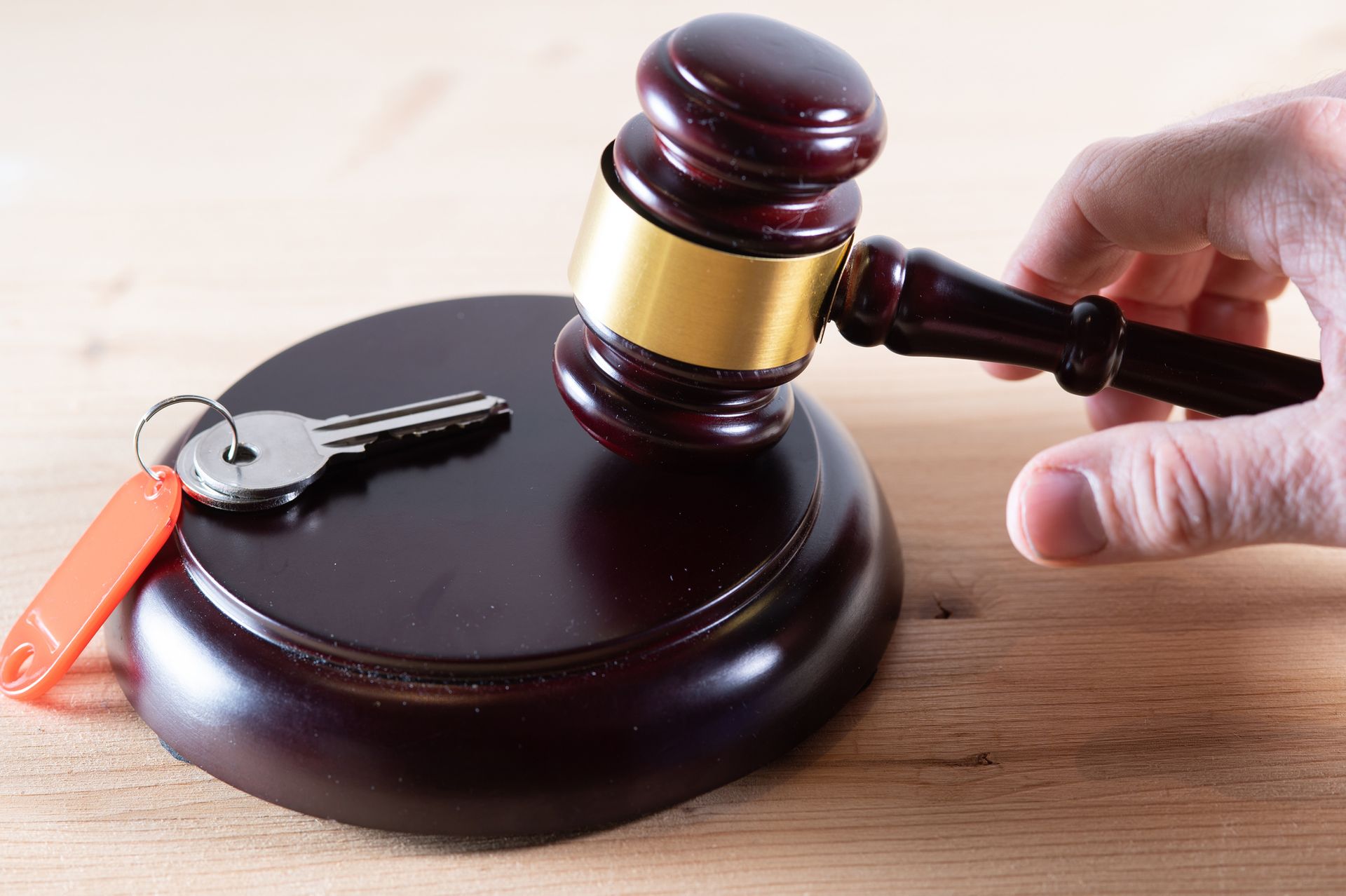 A person is holding a wooden gavel next to a key on a wooden table.