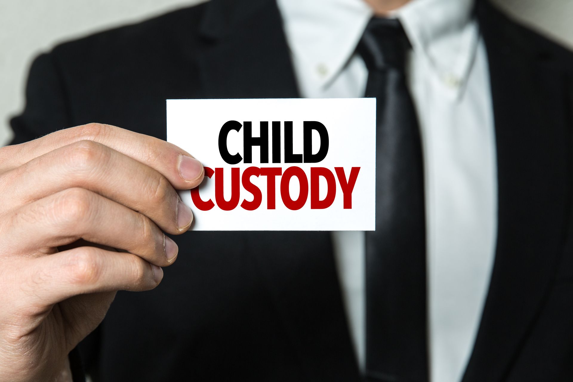 A man in a suit and tie is holding a card that says child custody.
