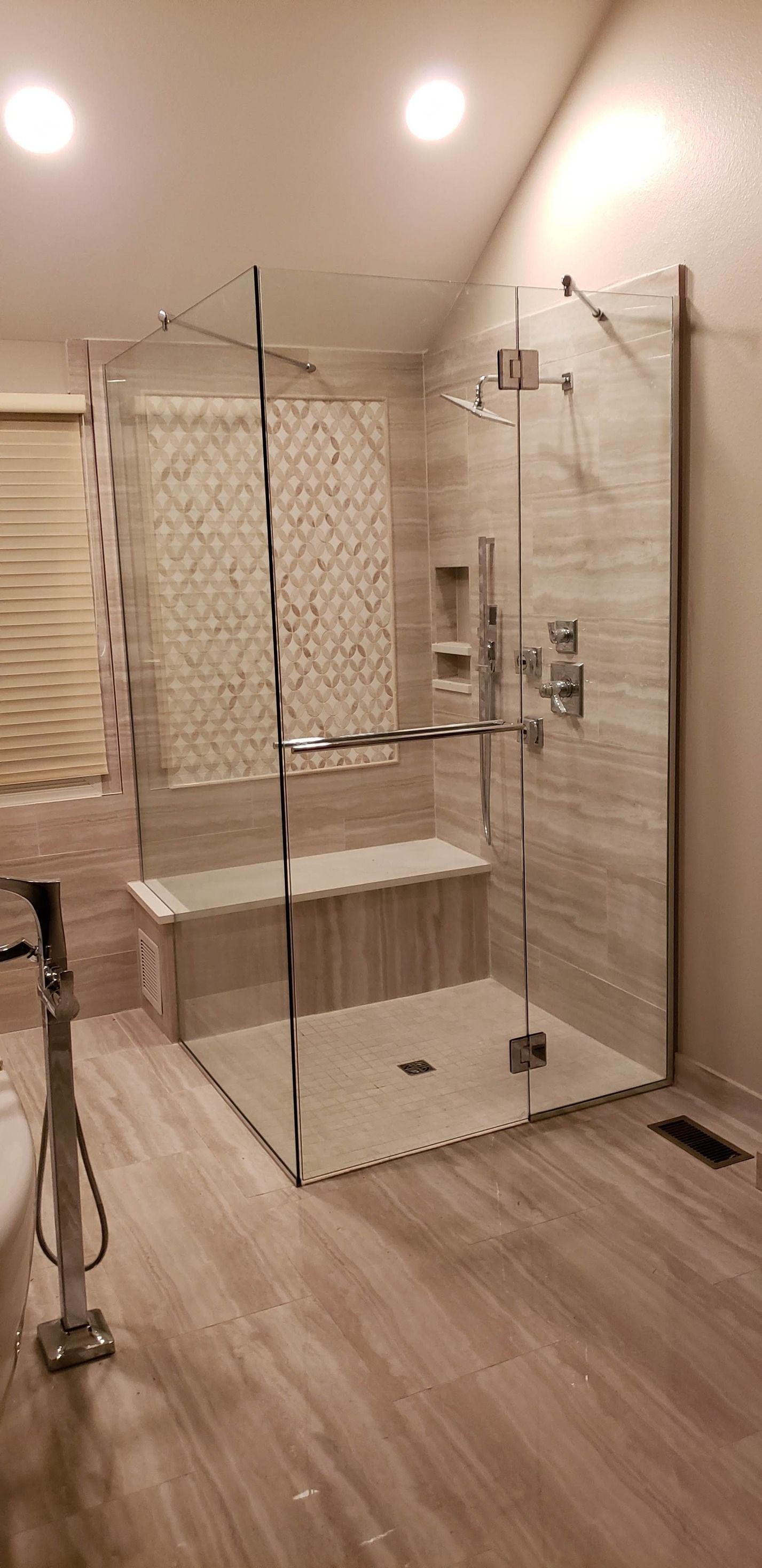 A luxurious glass shower with a bench seat and gray tile. The shower is in a bathroom with light brown flooring.